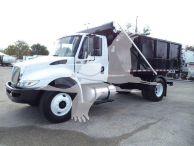 Truck in-service International Durastar 4300 roll-off truck with dump bed, cab interior not visible, side view showing front wheel and rear container.