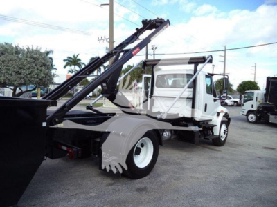 International Durastar 4300 rolloff truck side view showing hydraulic arms and dumping bed, white cab with black chassis.
