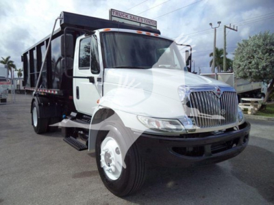 International Durastar 4300 roll-off truck in white and black, front three-quarter view, chrome grille, dual rear bed, dealer lot in background.