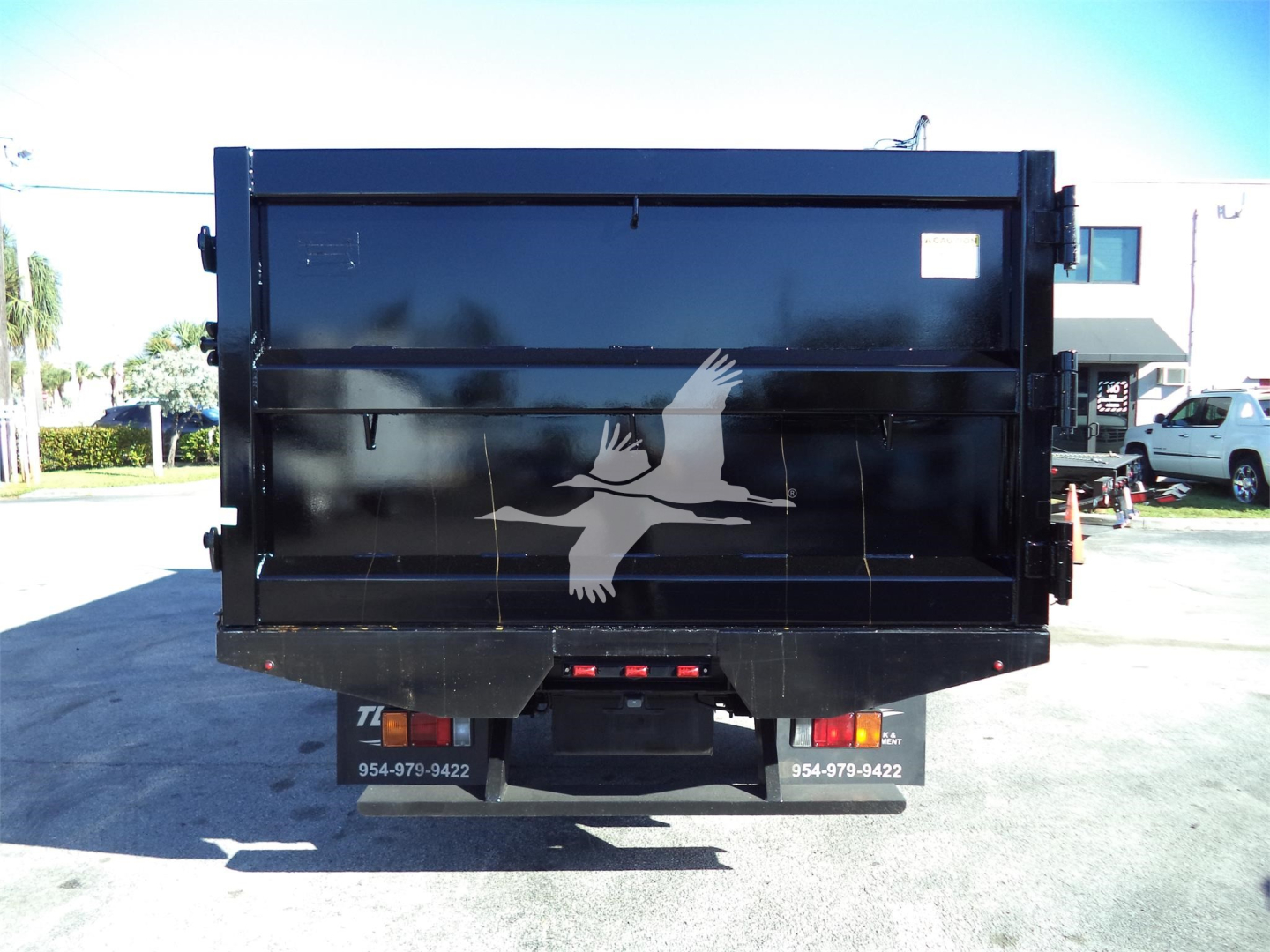 Back view of a black Isuzu dump truck bed with a white bird logo, in a parking lot.
