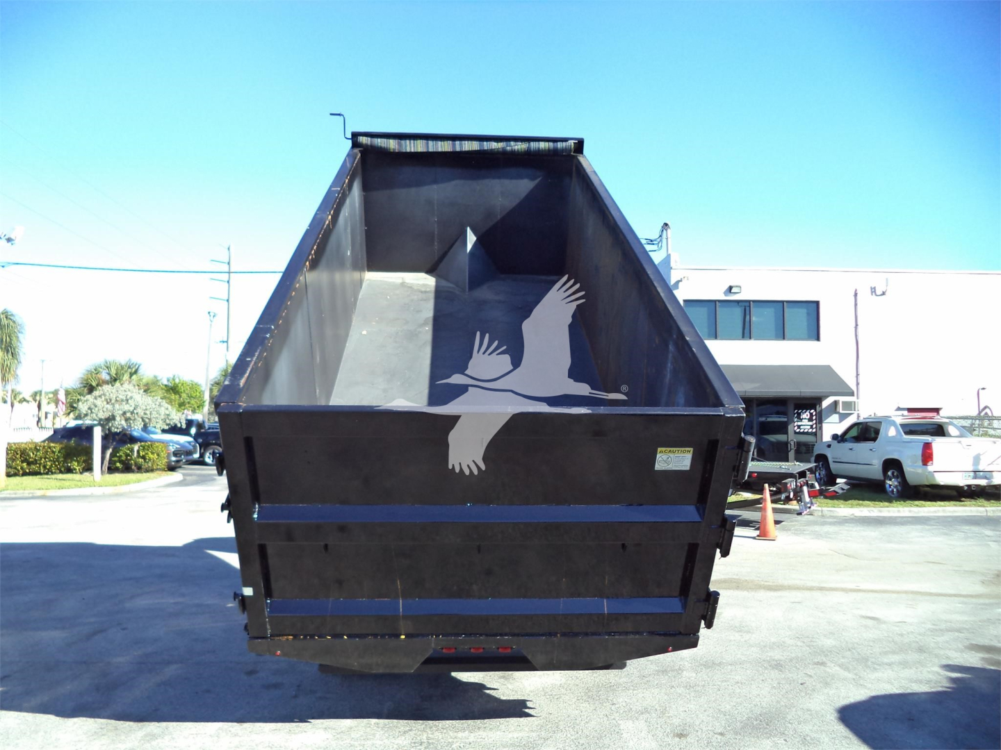 Dump truck bed of a Isuzu NRR dump truck with open tailgate, lot in background.