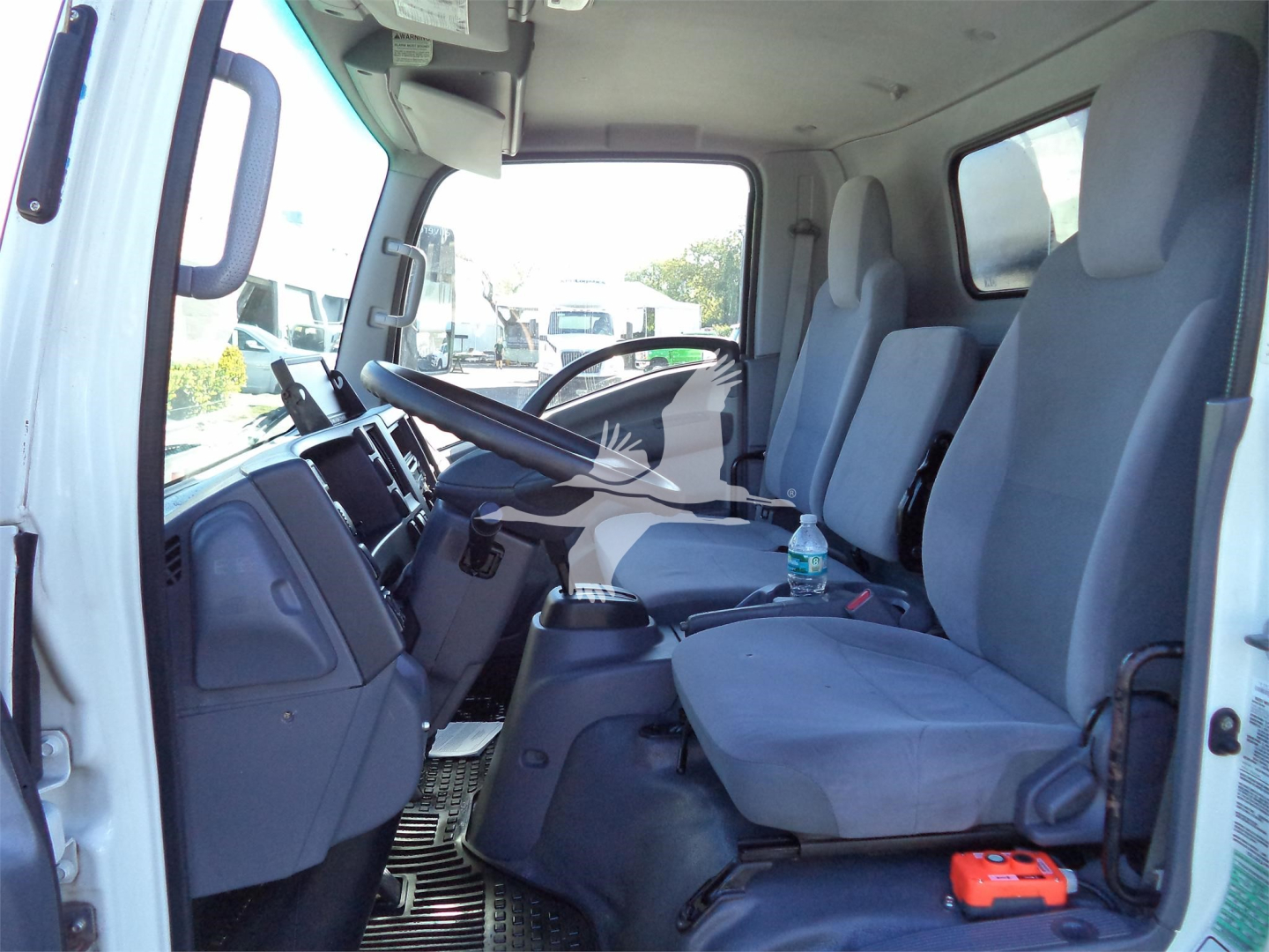 Isuzu NPRR cab interior showing driver and passenger seats with dashboard, steering wheel, and gear area.