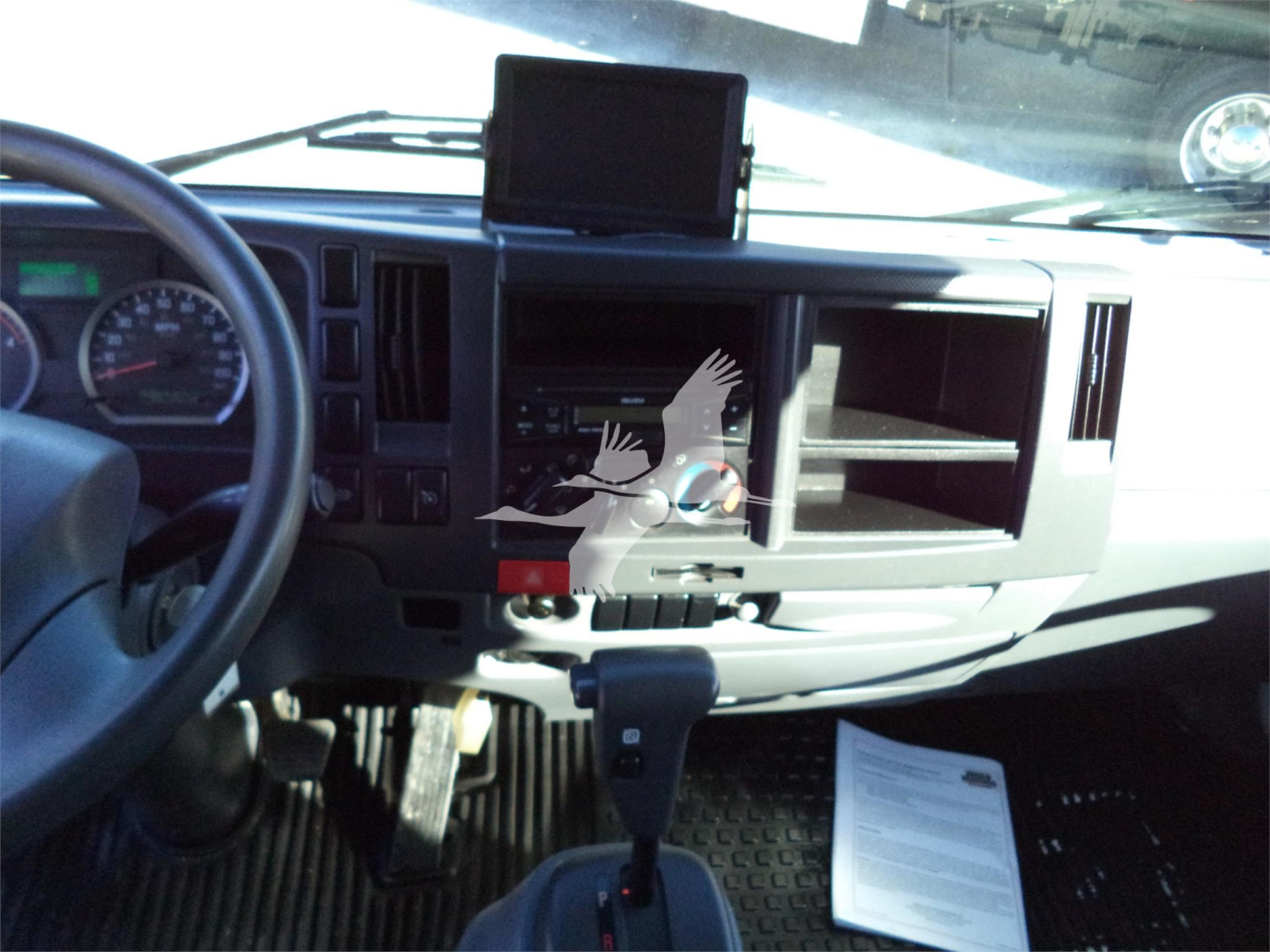 Isuzu NPRR cabin dashboard and steering wheel view showing center console with open radio slot, gear lever, and a mounted tablet display on the dash.