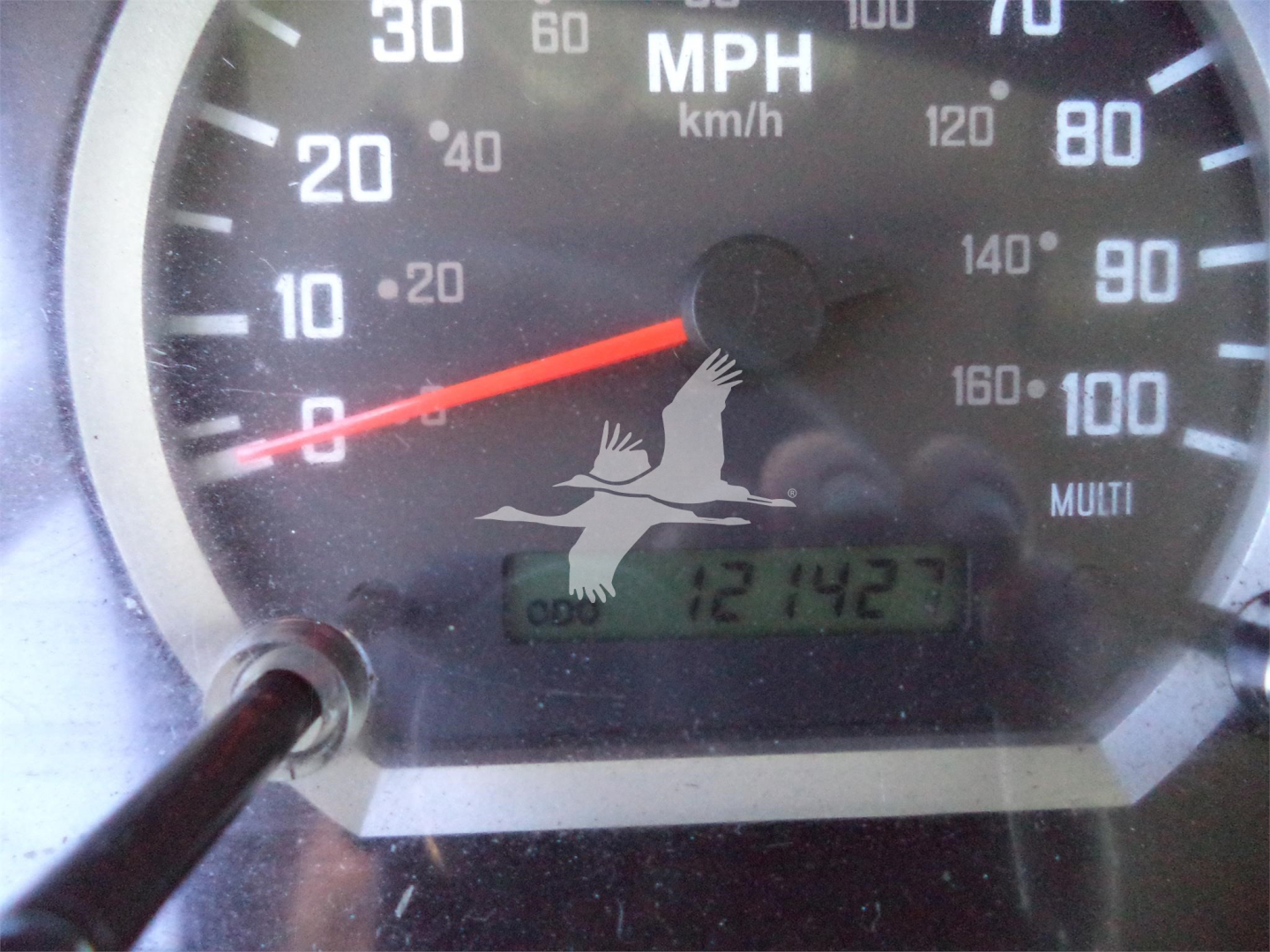 Dial gauge showing speedometer with needle near 0 and digital odometer reading 121427 miles on Isuzu truck dashboard.