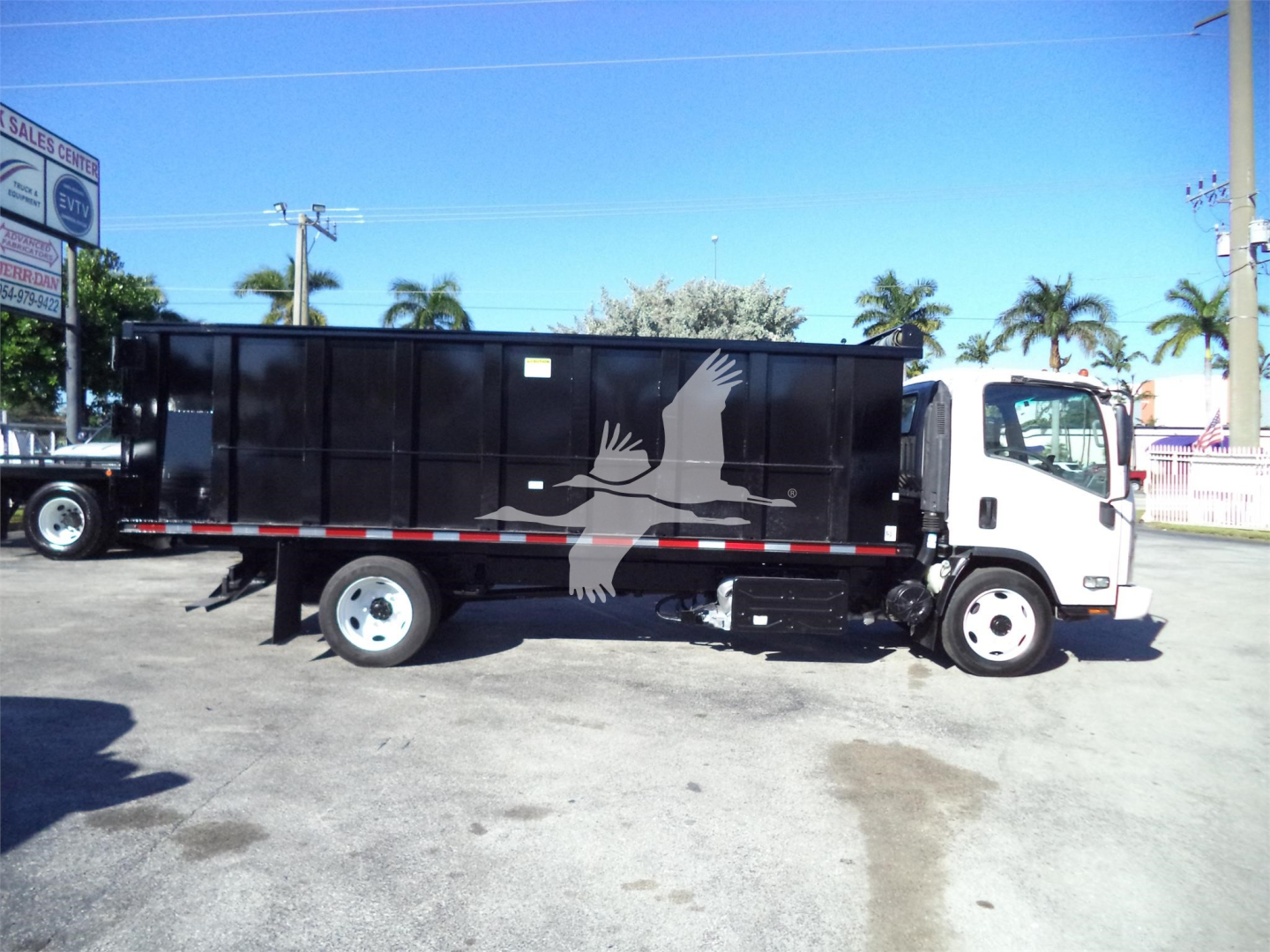 Isuzu NPRR dump truck in service with black dump body showing white bird graphic on side.