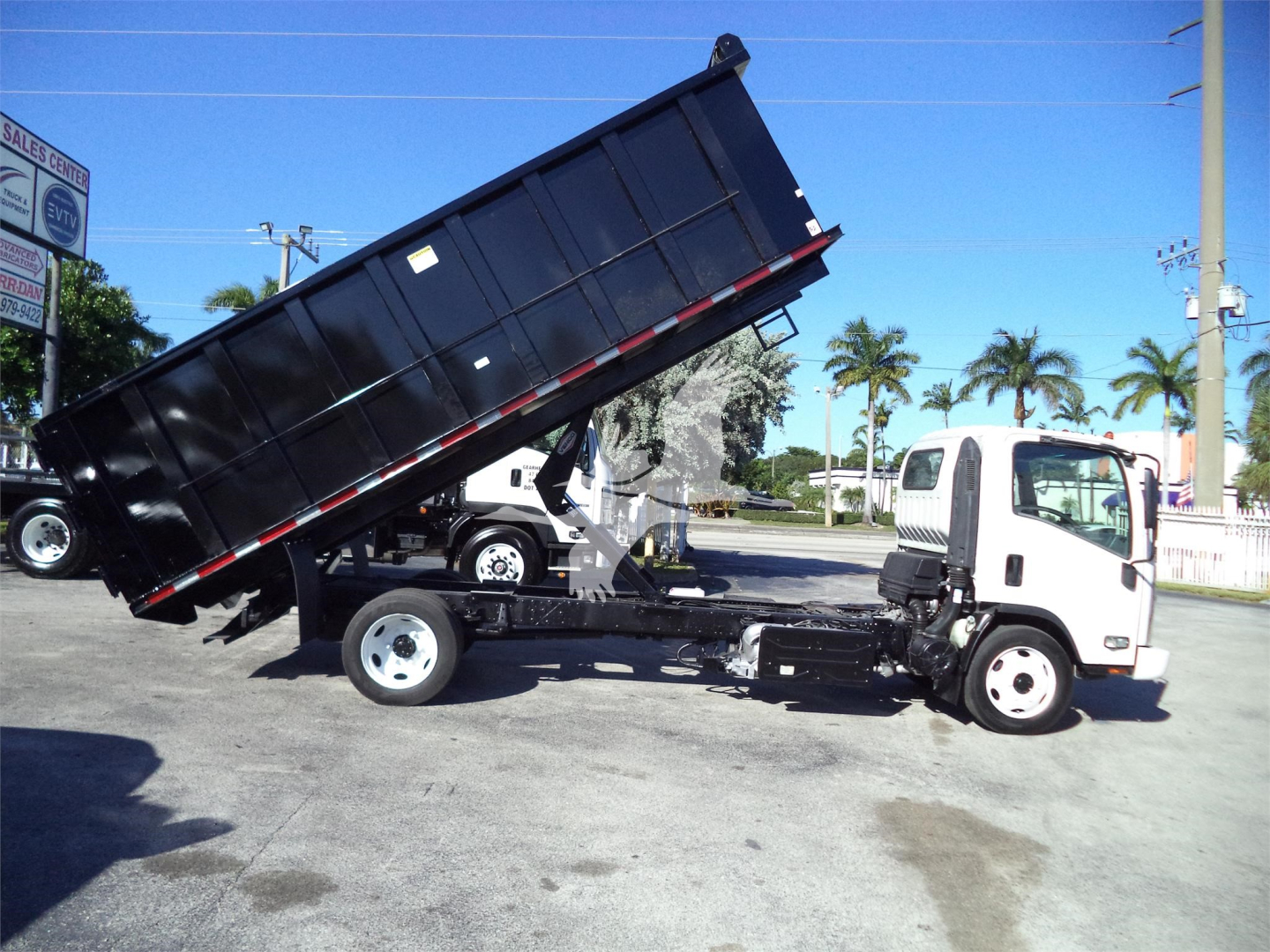 Isuzu NPRR dump truck in-service showing a raised dump bed on a white cab, with black dump body and dual rear wheels.