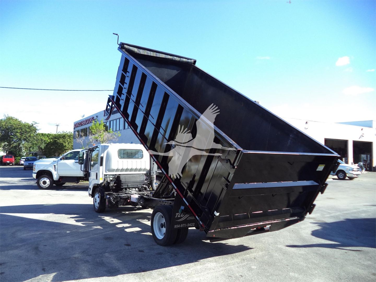 Isuzu NPRR dump truck with lifted black steel dump bed in a dealership lot.