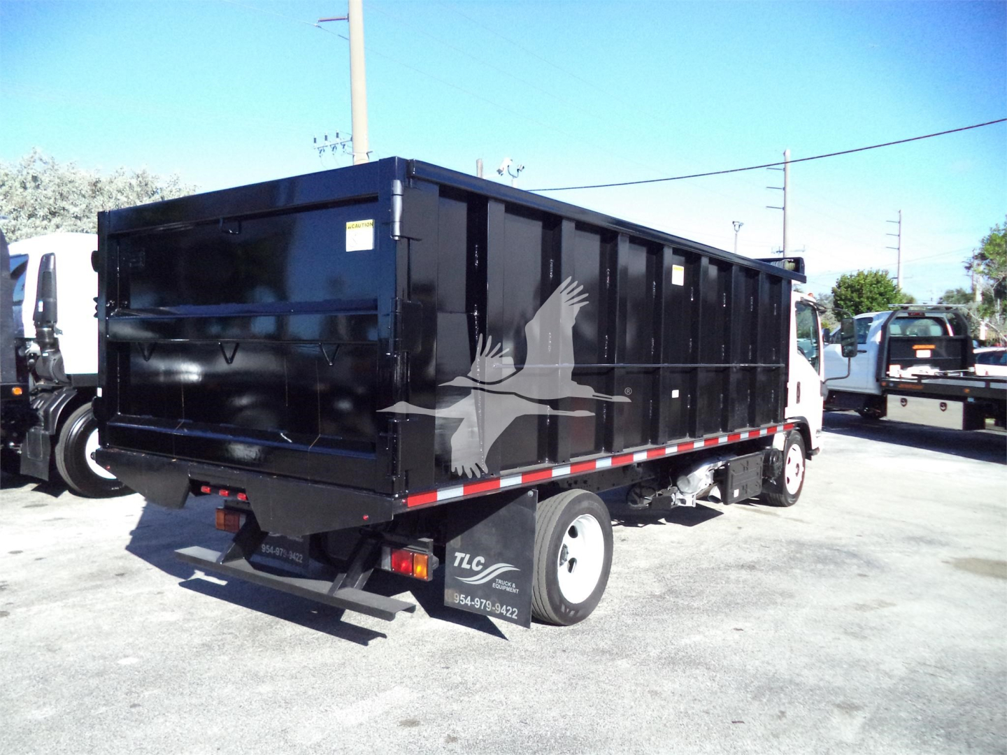 Isuzu NPRR dump truck bed side and rear showing solid black dump body with white bird graphic.