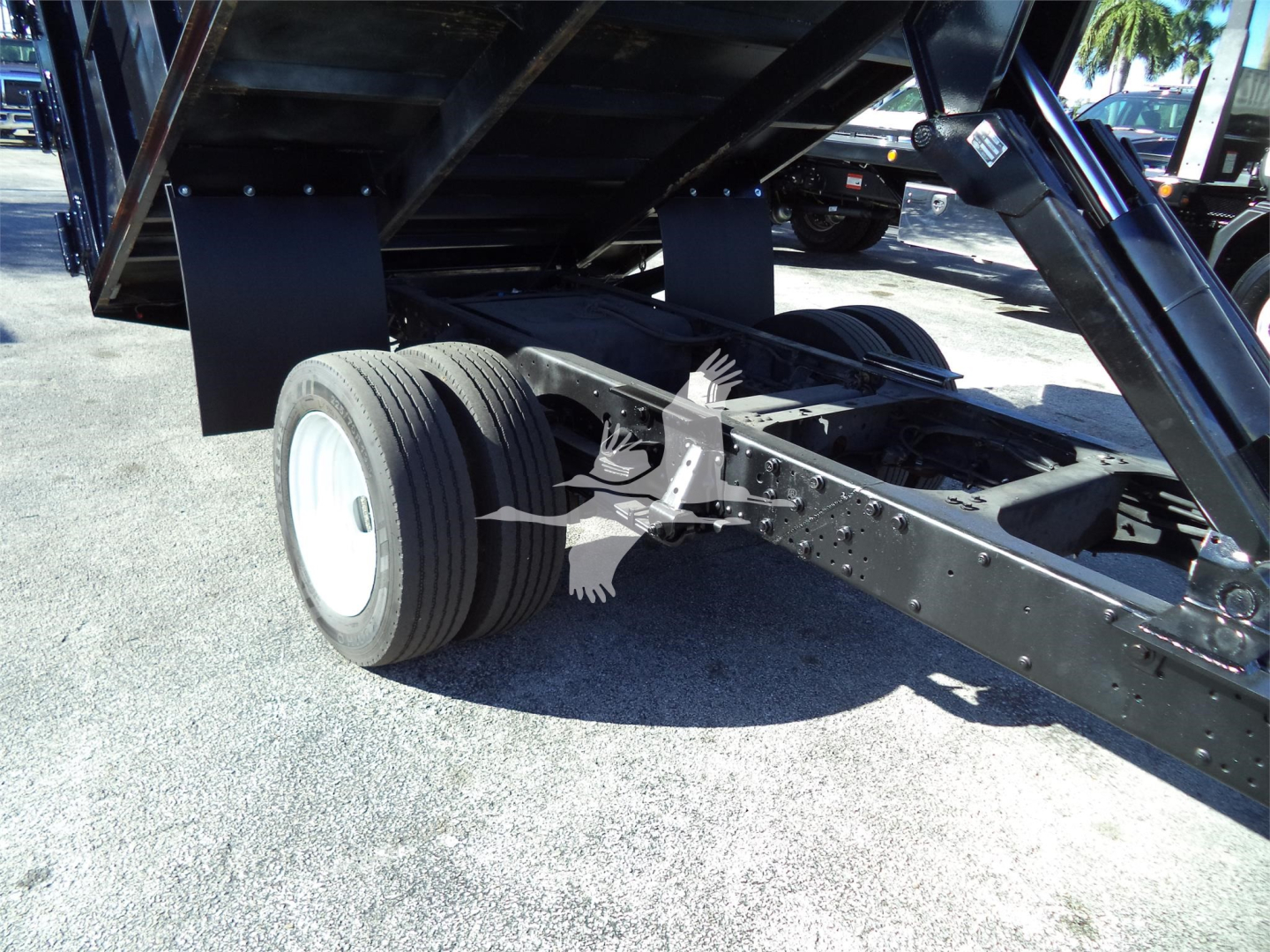 Isuzu NPRR dump truck chassis and rear dual wheels with dump bed lifted, showing suspension and axle components.