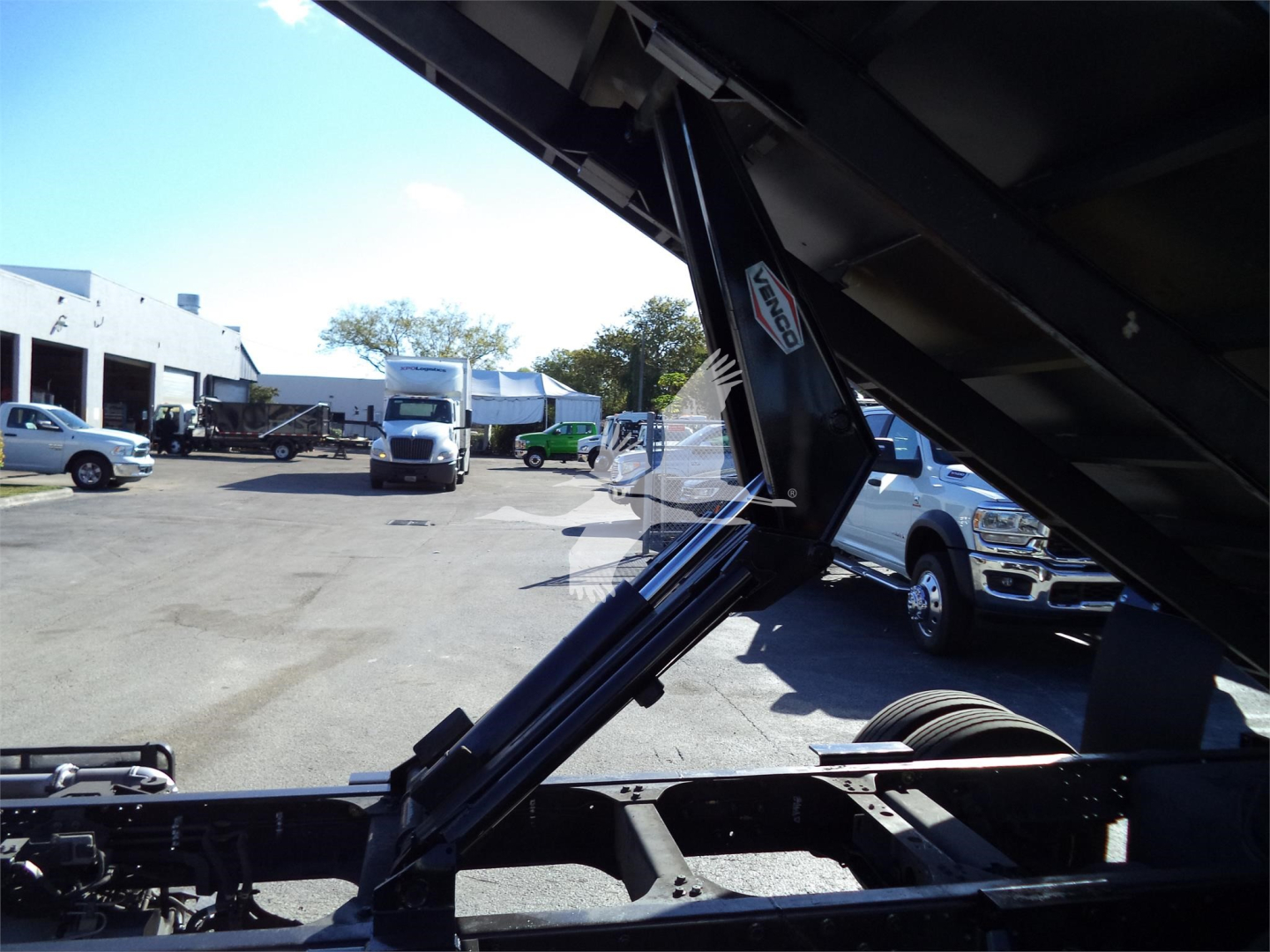 Isuzu NPRR dump truck chassis with hydraulic dump bed in view, showing hydraulic cylinders and frame components.
