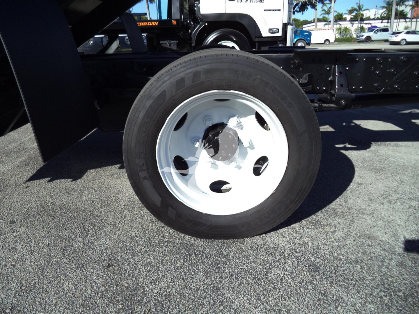 Isuzu NRR dump truck wheel/view showing front tire and white steel rim with bolts, undercarriage and frame in background.