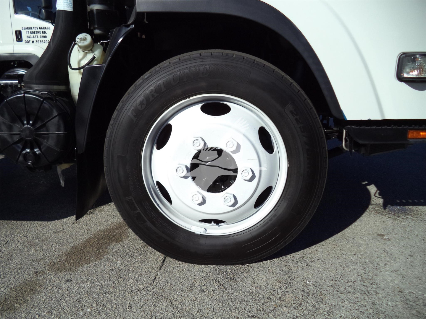 Isuzu NPRR front wheel showing steel wheel with central plastic hub and lug nuts, part of dump truck chassis