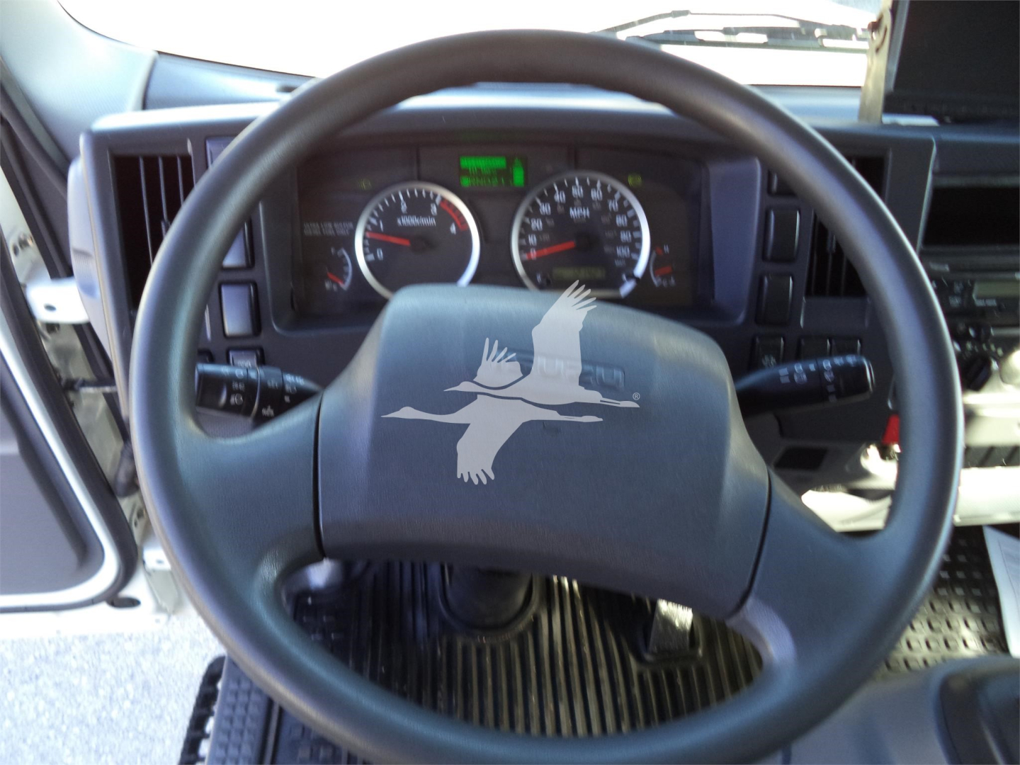 Isuzu truck cockpit showing steering wheel with logo and gauge cluster in dashboard.
