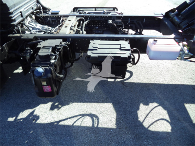 Isuzu NPRR chassis showing battery, air tanks, and hydraulic lines under truck frame with fuel lines and wiring.