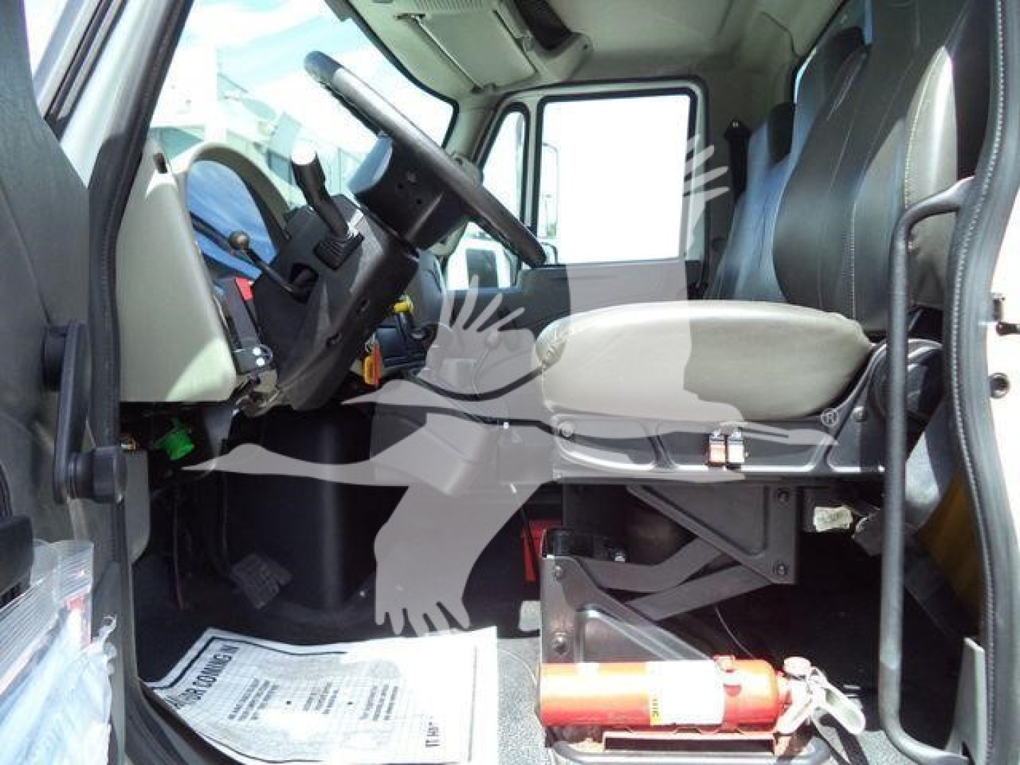 Cab interior of a 2019 International 4300 dump truck showing driver seat, steering wheel, and dashboard, with floor mats and a fire extinguisher nearby.