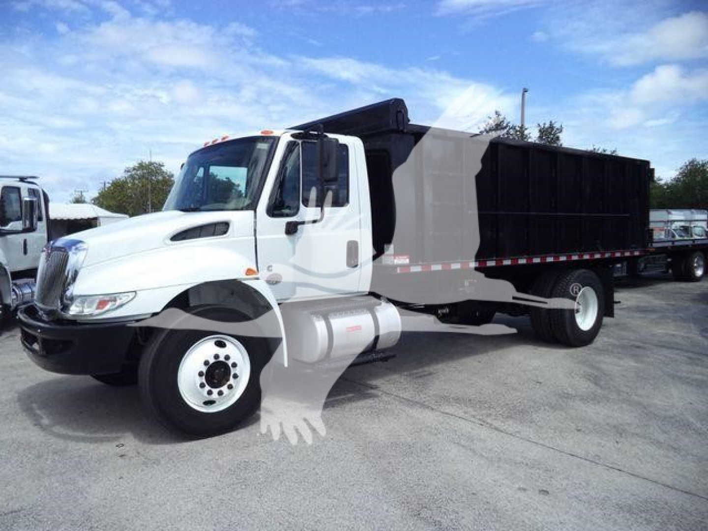 International dump truck with white cab and black dump body, side view in lot.