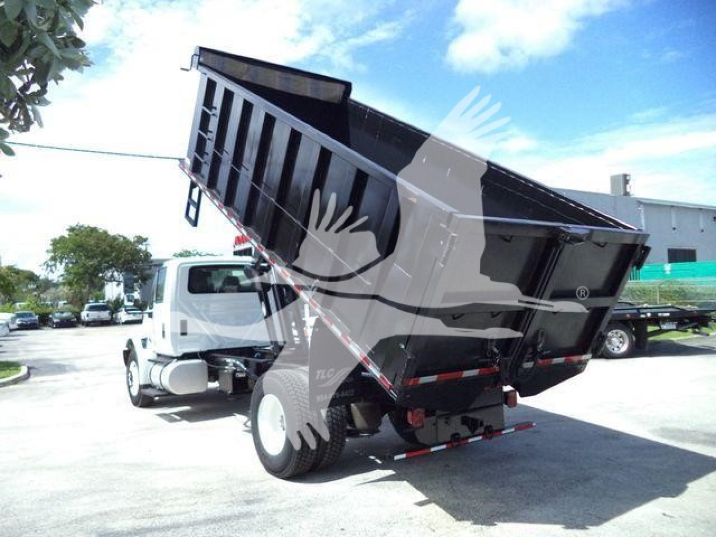 Dump truck in-service with raised dump bed on International 4300 chassis, black bed, white cab, rear view showing hydraulic lift and tires.
