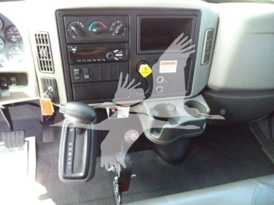 Cab interior of a 2019 International 4300 dump truck showing dash with HVAC controls, radio, empty display, gear selector on the column, and pedals; yellow warning tag and a console area.
