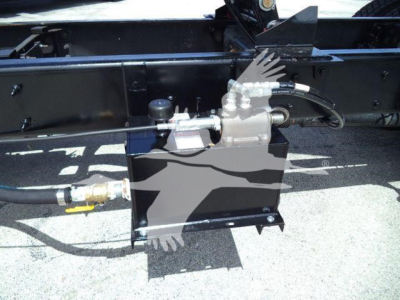 Industrial truck component showing hydraulic pump and hoses mounted on a black metal frame with fittings and a small reservoir.