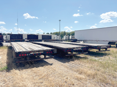 Flatbed trailers in a lot; rear view showing multiple Transcraft DTL-2100 trailers with deck planks, taillights, and tandem axles.