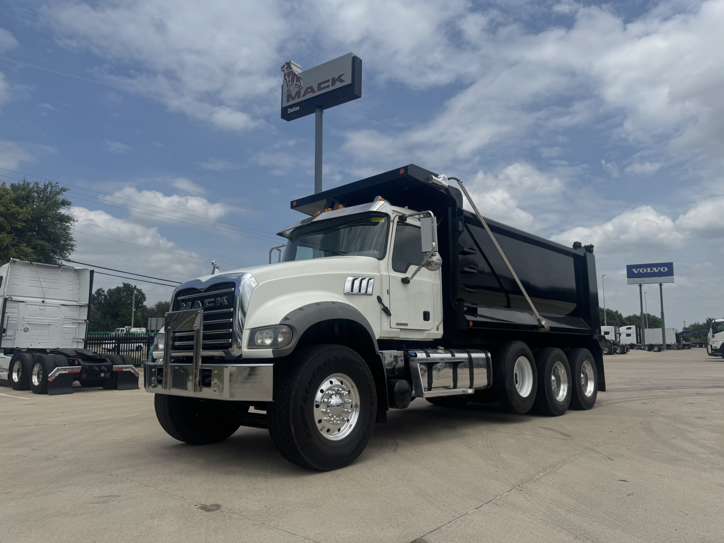 Truck: 2021 Mack GR64F dump truck, white cab with black dump body, front grille, large mirrors, six wheels visible, dealership lot in background.