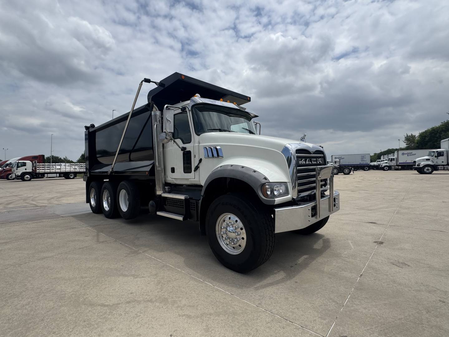 Truck image showing a white 2021 Mack GR64F dump truck with six wheels and a raised dump bed in a parking lot.