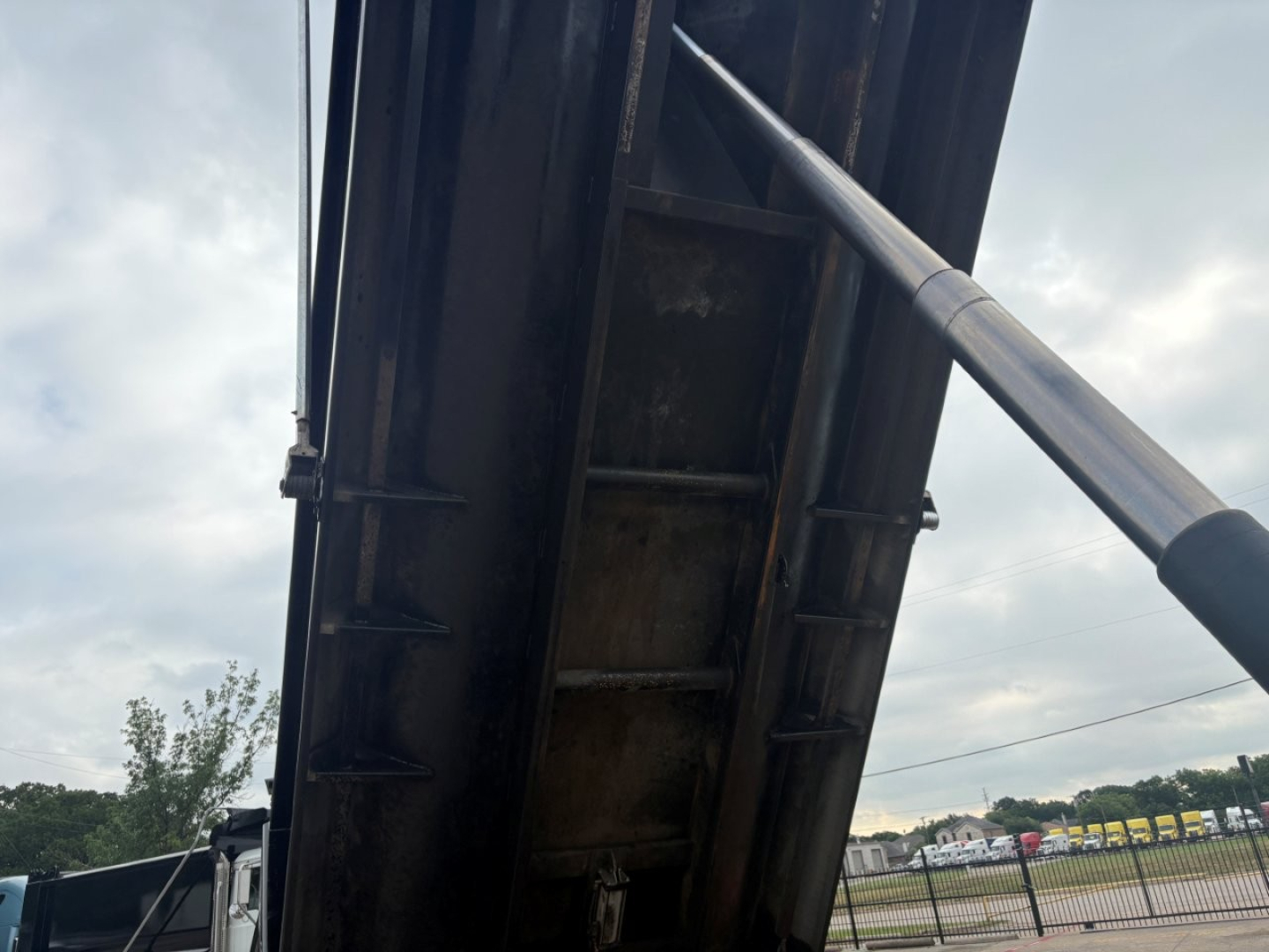 Dump truck bed interior with hydraulic cylinder and metal side wall showing a portion of the Mack GR64F undercarriage.