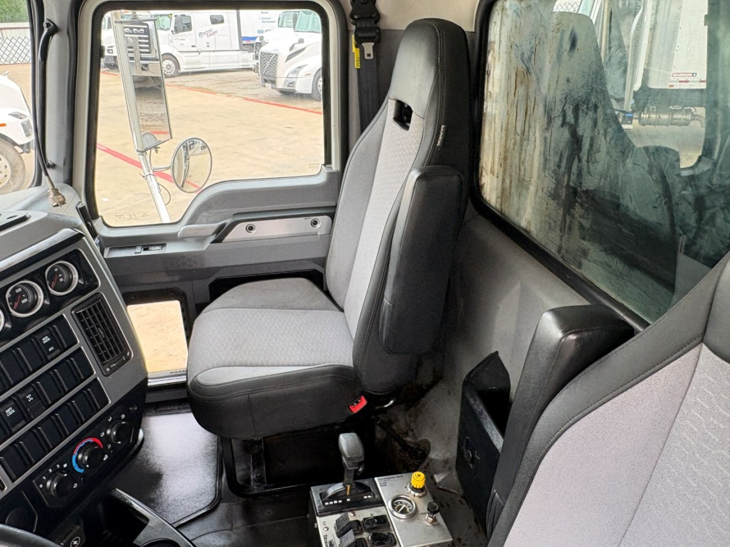 Cab interior of a 2021 Mack GR64F dump truck showing driver seat and passenger seat, steering wheel, dashboard, center console, gear selector, and window with side mirror.