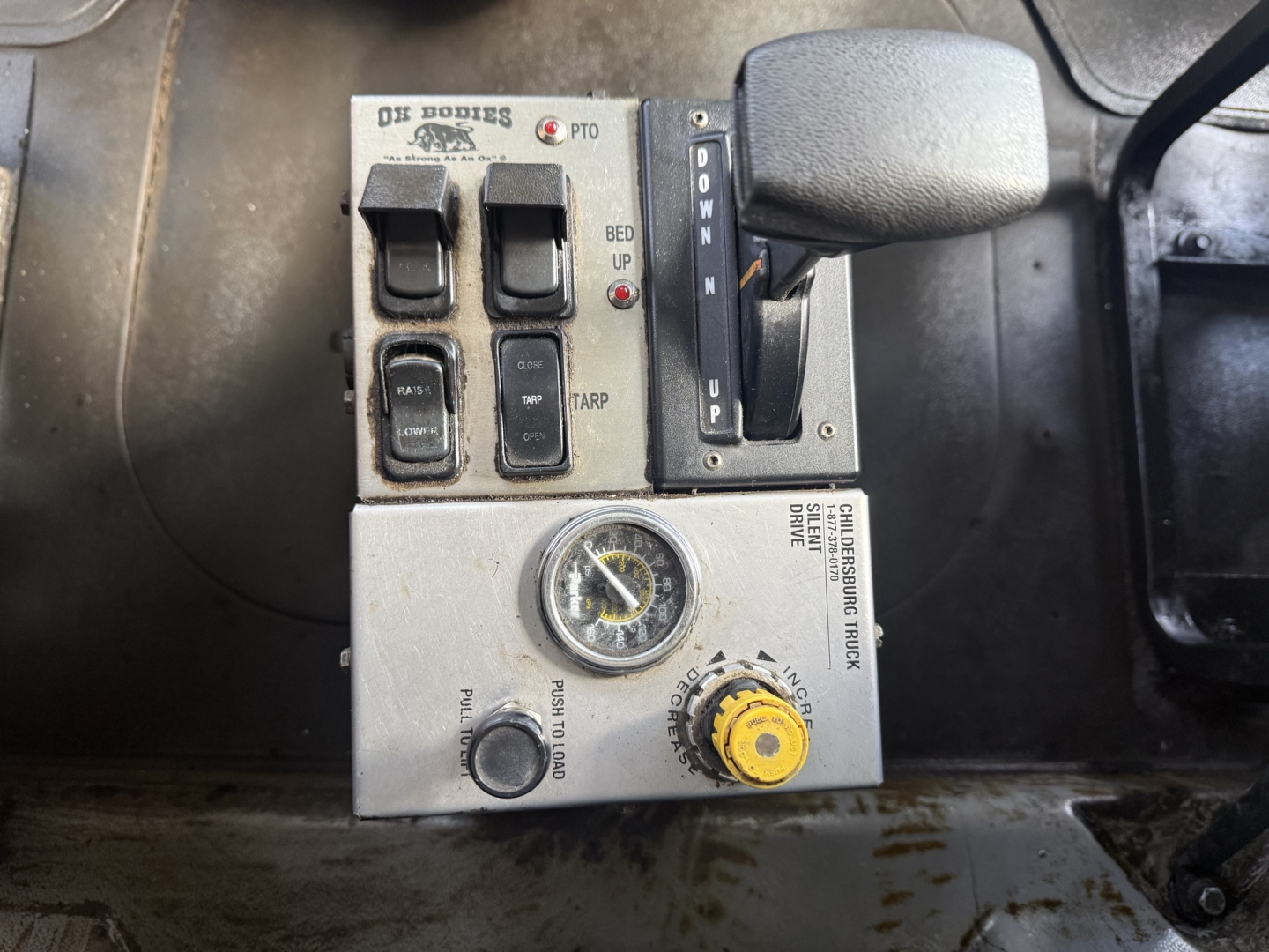 Mack GR64F control panel with switches and gauges showing PTO, throttle, and gear selector in cab interior.