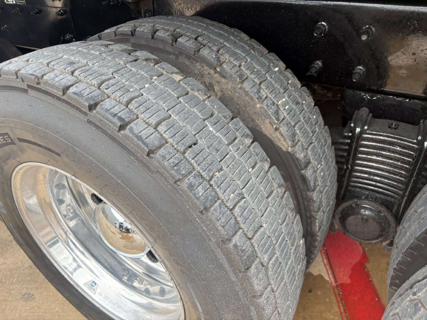 Mack GR64F truck rear dual tires and suspension components with chrome wheel, visible leaf springs, and chassis undercarriage.