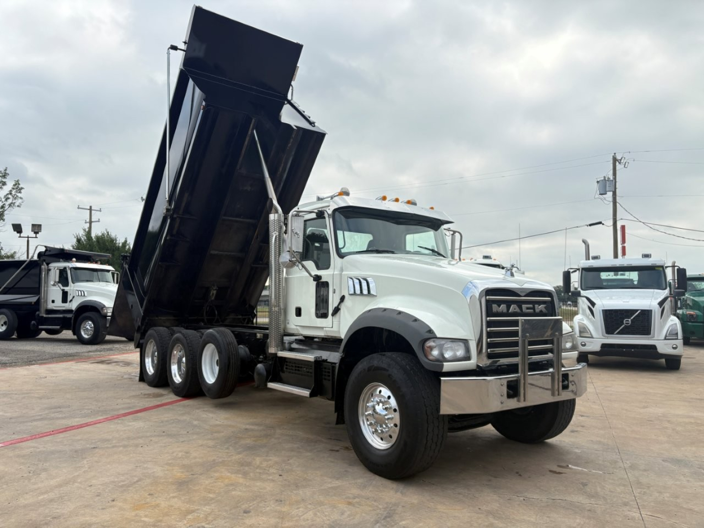Mack GR64F dump truck in-service with white cab and black dump body raised, showing dual rear axles and chrome front bumper.