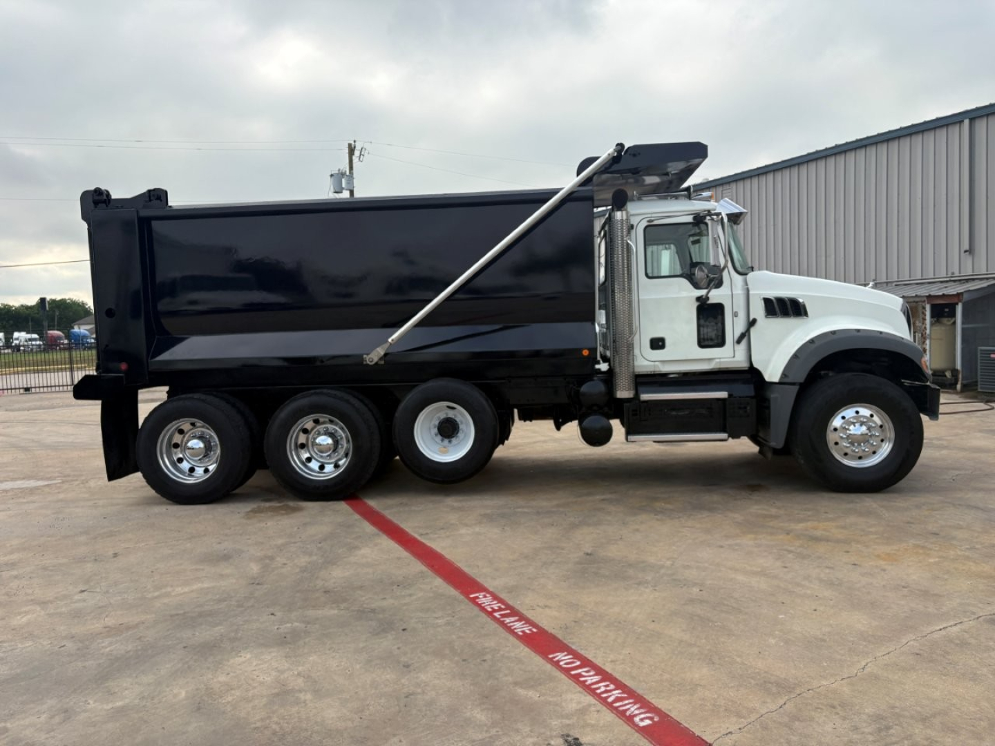 Mack GR64F dump truck side view showing front cab, black dump bed, and three rear axles with chrome wheels.