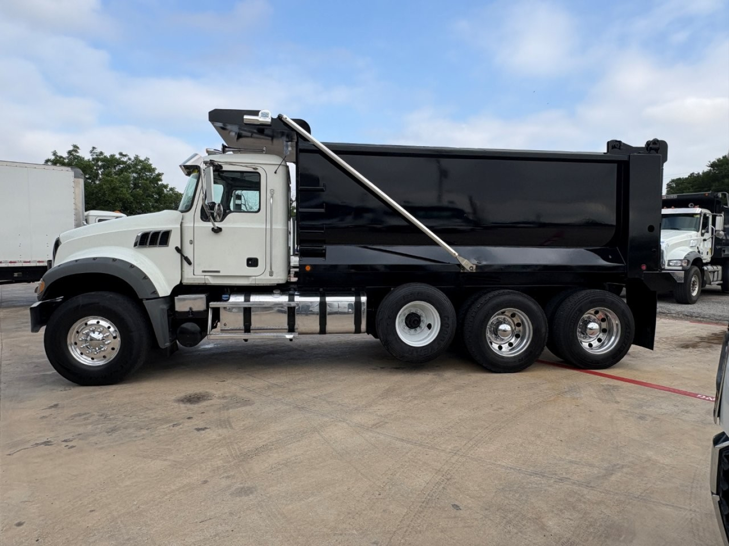 Dump truck side view showing 2021 Mack GR64F with black dump bed and white cab.