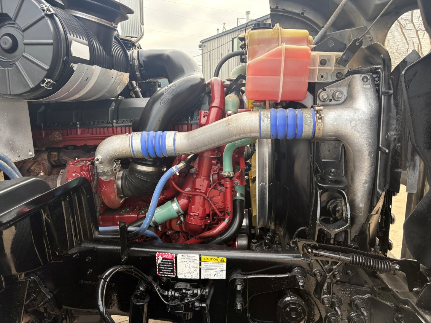 Mack GR64F engine bay showing coolant reservoir and blue silicone hoses with an orange/red engine component in a used truck.
