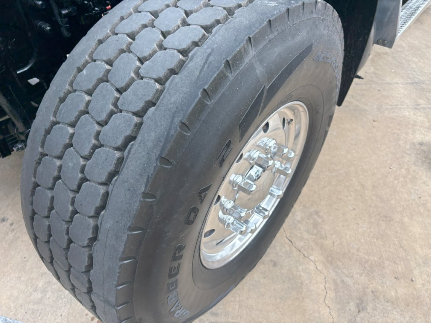 Steer-side front dual rear tire on a Mack GR64F dump truck showing Goodyear tire with tread pattern and polished aluminum wheel.