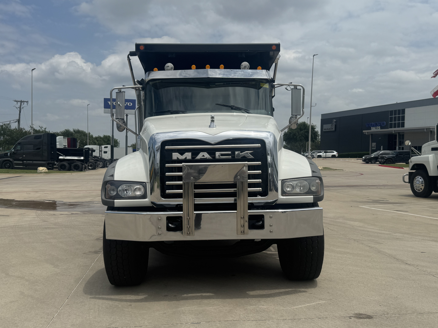 Front view of a white 2021 Mack GR64F dump truck showing prominent Mack grille, bumper, and dual steel braces; headlights and windshield visible.