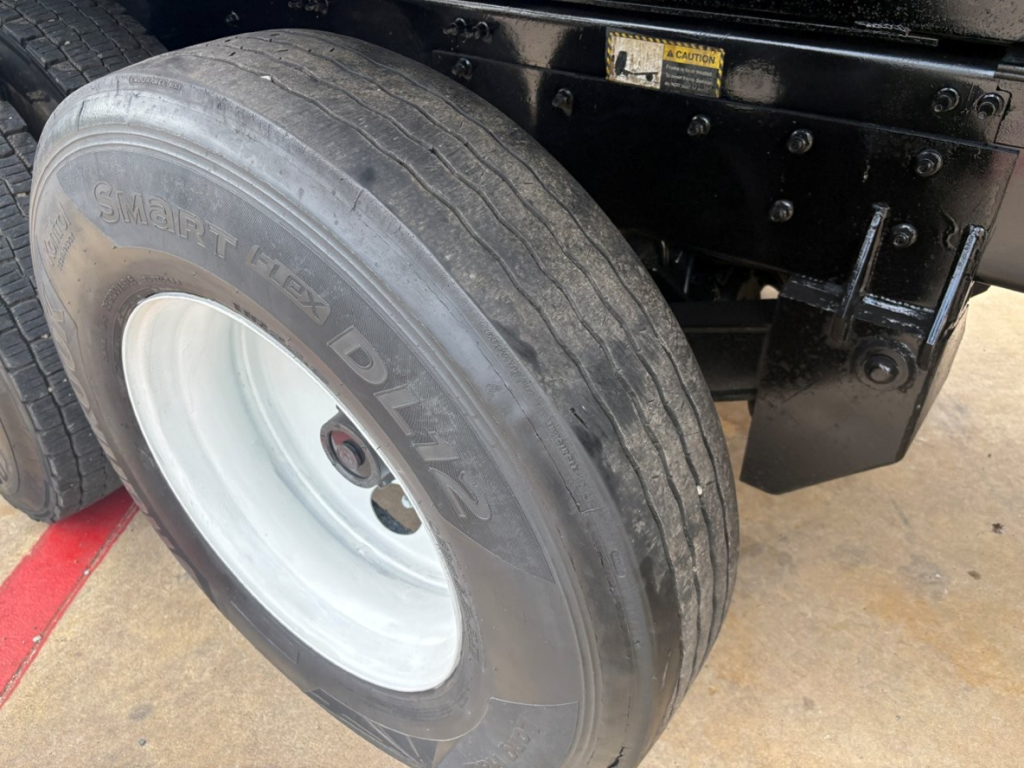 Mack GR64F truck front wheel and suspension area showing tire and wheel with visible rim and part of chassis.