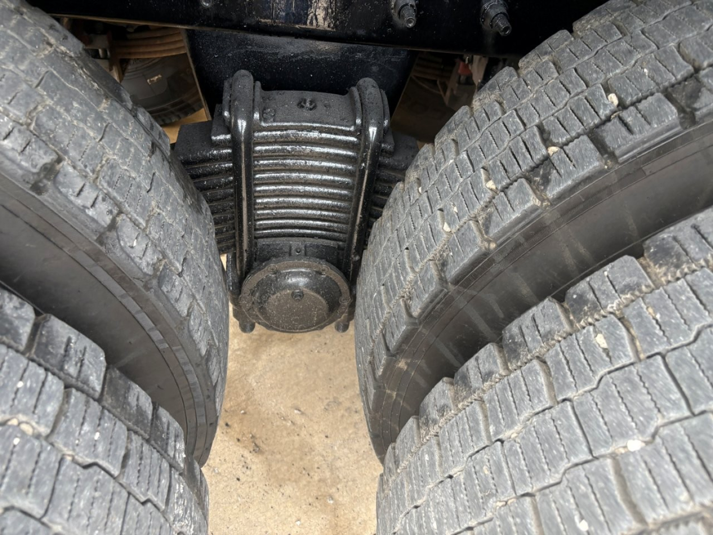 Rear dual rear axle suspension of a Mack GR64F dump truck with heavy-duty leaf springs between dual tires.