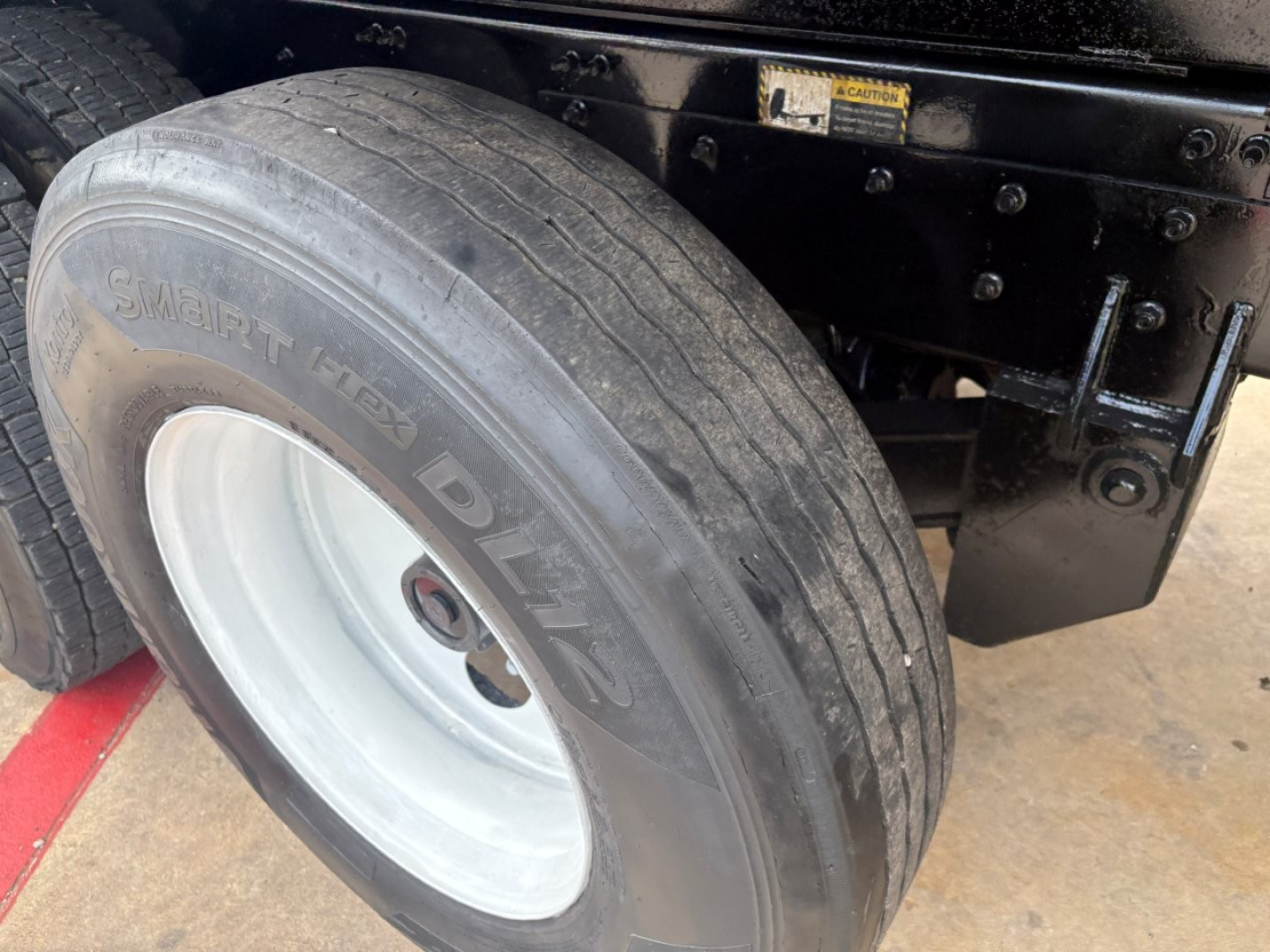Mack GR64F dump truck wheel and fender area with Smart Flex Duals tire and white wheel, undercarriage frame visible.
