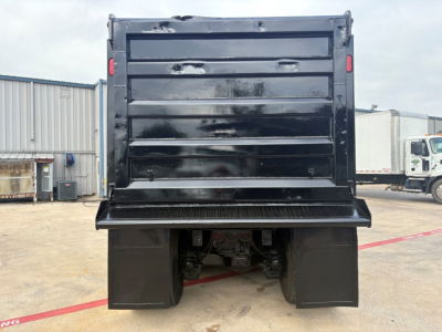 Dump truck bed showing rear view of Mack GR64F with black dump body and undercarriage components visible.