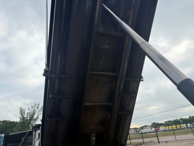 Dump truck bed interior with hydraulic cylinder and metal side wall showing a portion of the Mack GR64F undercarriage.