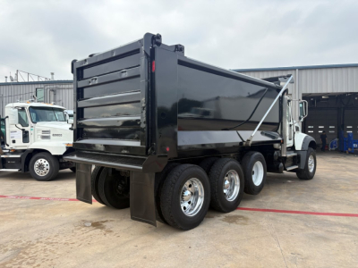 Dump truck rear three-axle chassis showing loading container and tires with Mack GR64F badge not visible.