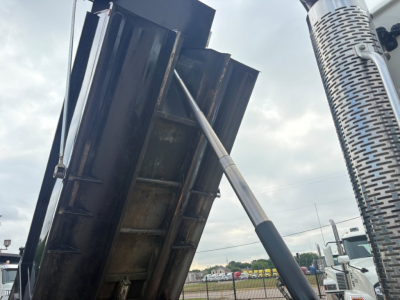 Dump truck bed with hydraulic arm in a raised position and a vertical exhaust stack visible.