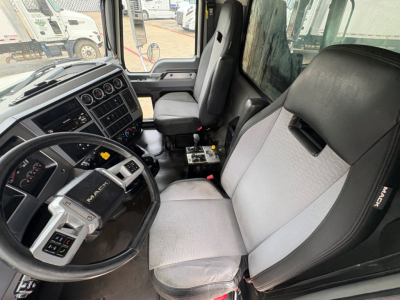 Mack GR64F truck cab interior showing steering wheel, dashboard controls, and driver seat with light gray fabric.