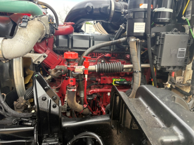 Engine bay of a Mack GR64F dump truck showing red engine block, red oil cap labeled STEP, hoses, and black plastic components.