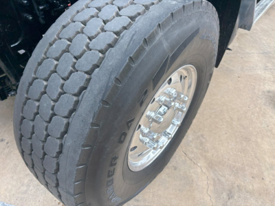 Steer-side front dual rear tire on a Mack GR64F dump truck showing Goodyear tire with tread pattern and polished aluminum wheel.