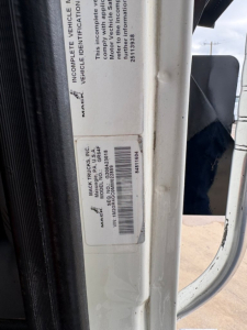 Label on Mack truck door showing VIN, stock number, and company information. Visible text includes 1M2GR4GC0MM022859, Stock No B3433P, INCOMPLETE VEHICLE, VEHICLE CERTIFICATE DOCUMENT, MACK TRUCKS INC, MACK TRUCKS, INC. and barcode area.