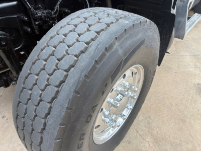 Truck tire and wheel of a Mack GR64F dump truck showing heavy-duty tread and chrome hub with lug nuts.