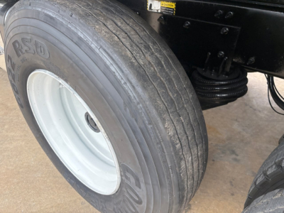 Mack GR64F wheel and front suspension view showing RSD tire with white steel rim and undercarriage components.