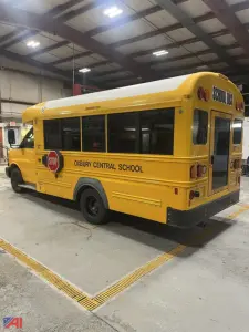 Rear three-quarter view of a yellow 2016 Chevrolet Express school bus inside a garage, showing 'OXBURY CENTRAL SCHOOL' lettering and STOP sign on side, black wheels, rear window, and roof lights.